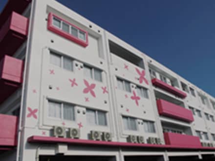 ピンク色のアクセントが施された介護施設の建物外観。晴天下の全体像。